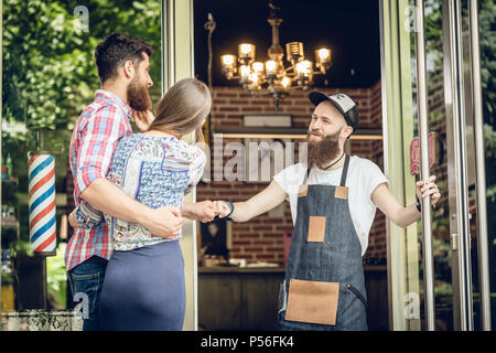 Cool hairstylist mit einer Faust bump zu einem glücklichen Kunden an der Tür Stockfoto