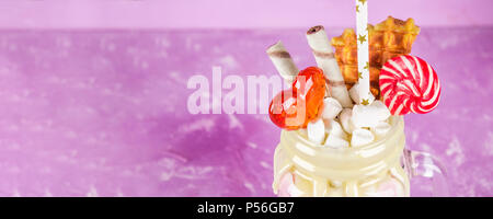 Freakshake von rosa Smoothie, Creme. Monstershake mit Lutscher, Waffeln und Eibisch. Extreme Milchshake in einem Marmeladenglas. Rosa lila Hintergrund. Stockfoto