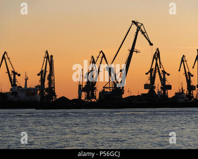 Das Meer und die dunklen Silhouetten von Cargo Cranes in der Hafenstadt auf der hellen orange Himmel bei Sonnenuntergang Stockfoto