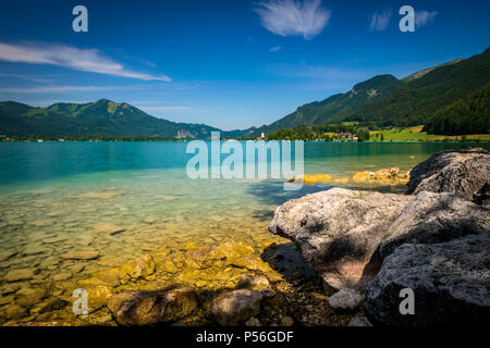 See namens Wolfgangsee in Österreich mit Steinen vor und die Berge im Hintergrund und Wolken am blauen Himmel Stockfoto