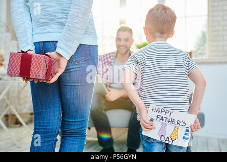 Zurück Blick Porträt der jungen Frau und kleinen Jungen überraschend Vati für Vatertag geben ihm Geschenke und handgemachte Grußkarte Stockfoto