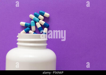 Gruppe der sortierten weißen und blauen Tabletten. Kapseln verschütten aus weiße Flasche. Violett unterlegt. Stockfoto