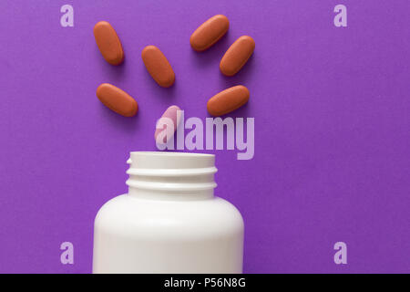 Alle Tabletten sind Rot, mit einer Ausnahme: Pink. Kapseln verschütten aus weiße Flasche. Violett unterlegt. Stockfoto