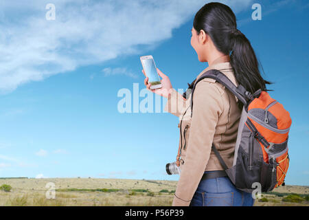 Junge asiatische tourist Frau Betrachten von Fotos auf Ihrem Smart Phone auf der Wiese Stockfoto