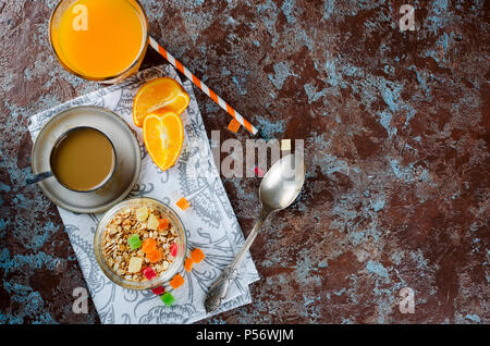 Gesundes Frühstück mit hausgemachtem Müsli in Glas Glas mit farbigen kandierte Früchte, Kaffee und Orangensaft auf dunklem Hintergrund Stockfoto