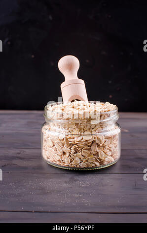 Haferflocken in Glas und Löffel aus Holz auf dunklen vintage Holz- Hintergrund, selektiver Fokus Kopie Raum, Low Key Stockfoto