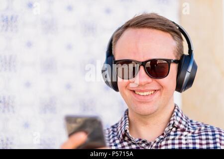 Junger Mann mit Bluetooth Kopfhörer angeschlossen in der Hand auf Smartphone Stockfoto