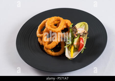 Gebratene Zwiebelringe mit gemüse salat auf einem schwarzen Platte Stockfoto