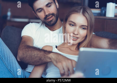 Die schöne Zeit zu Hause. Schöne junge Liebende Paar kleben aneinander und lächelnd, während Frau mit Buch Stockfoto