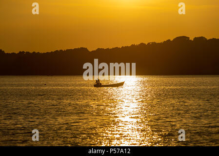 Sonnenuntergang über Brownsea Island, Poole Harbour, Dorset, England, Großbritannien, 25.. Juni 2018, Wetter: Einer der heißesten Tage des Jahres, als sich eine Hitzewelle im Süden etabliert. Zwei Männer in einem kleinen Fischerboot werden von der untergehenden Sonne beschildert. Stockfoto