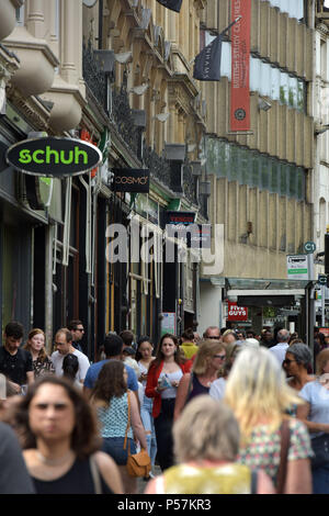Käufer und Touristen zu Fuß entlang Magdalen Street, Oxford, wo High Street Einzelhändler wie Supermärkte Sainsbury's Lokale, Tesco Metro, der Schuh r Stockfoto