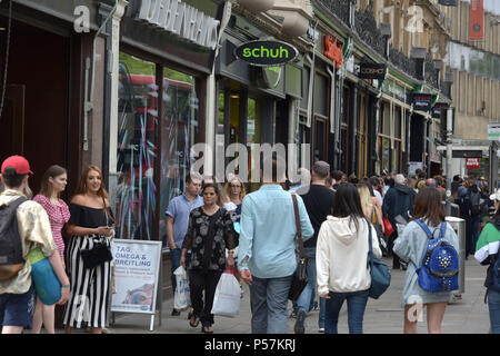 Käufer und Touristen zu Fuß entlang Magdalen Street, Oxford, wo High Street Einzelhändler wie Supermärkte Sainsbury's Lokale, Tesco Metro, der Schuh r Stockfoto