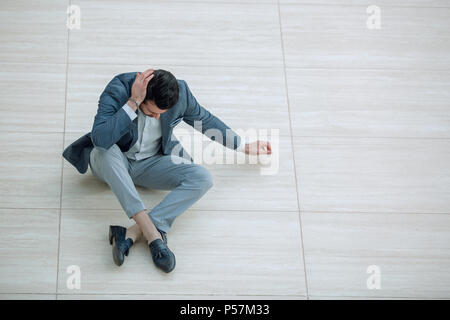 Frustrierte junge Unternehmer sitzen auf dem Boden und blickte nach unten. Stockfoto