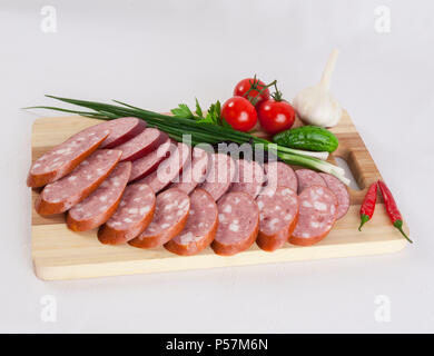 Stillleben mit in Scheiben geschnittenen geräucherten Wurst Grüns und Tomaten auf einem weißen Hintergrund. Kann für Banner und Außenwerbung und für Web site Desig verwendet werden. Stockfoto