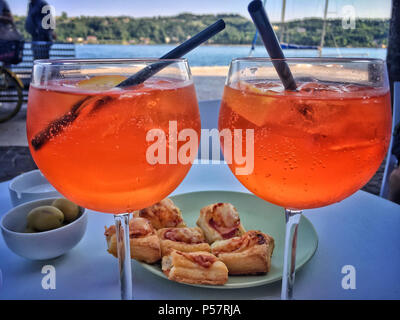 Zwei Gläser Aperol Spritz trinken mit ein paar Snacks auf einem Tisch vor dem Gardasee Stockfoto