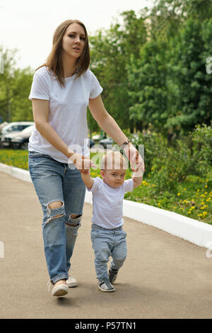 Familie. Mutter und Sohn gehen herum Park halten sich an den Händen. Schwangere Mädchen hilft kleinen Jungen laufen lernen. Stockfoto