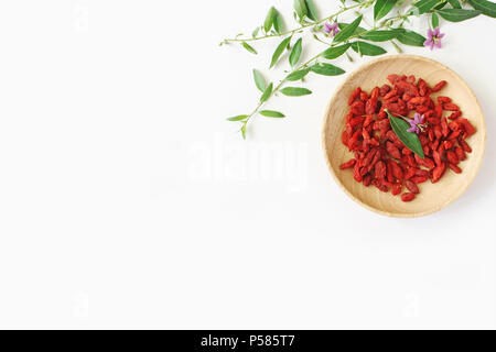 Haufen von getrockneten Goji Beeren Obst, Lycium Barbarum in Houten auf weißer Tisch. Blühende wolfberry pflanzliche Anlage Ast. Gesunde superfood. Flatlay, Ansicht von oben. Stockfoto