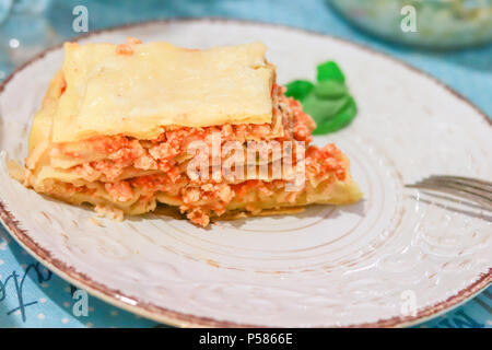 Lasagne Bolognese Schicht auf einem weißen gemusterten Platte mit Basilikum und die Gabel am Tisch Stockfoto