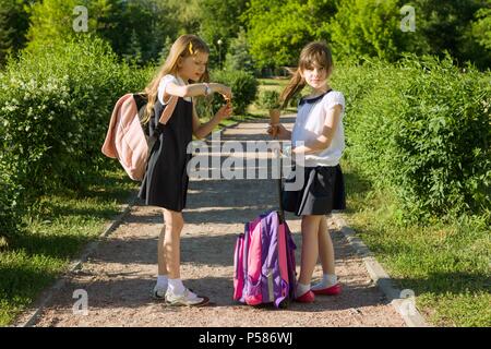 Ansicht der Rückseite zwei Schulmädchen Freundinnen mit Rucksäcken Eis essen. Stockfoto