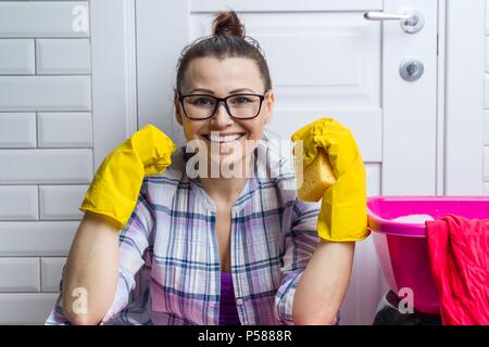 Professionelle Reinigung. Frau Hausmädchen in gelbe Gummihandschuhe mit Detergenzien lächelnd gegen weisse Türen Stockfoto