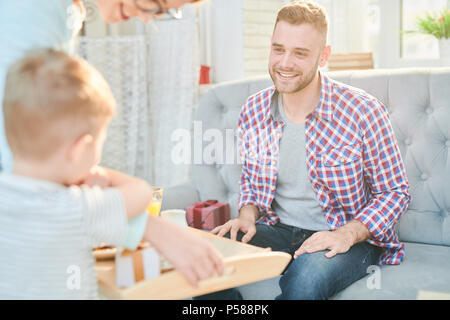 In warmen Farbtönen Portrait von gutaussehenden jungen Mann liebevoll an seine Familie suchen, lassen Sie sich überraschen Frühstück für Vatertag zu Hause, Kopie Raum Stockfoto