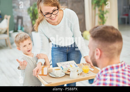 In warmen Farbtönen Portrait von Frau und Sohn bringen Überraschung Frühstück für Papa Vatertag zu Hause feiern. Stockfoto