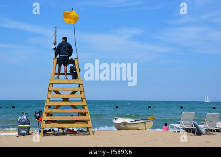 Ein Rettungsschwimmer wacht aus einem Wachturm an der North Avenue Beach in Chicago an einer gelben Flagge Warnung von rauhem Wasser Bedingungen. Stockfoto