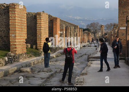 Die Besucher nehmen Bilder auf den traditionellen Fußgängerüberwege mit Lücken für den Wagen auf der Straße mit Kopfsteinpflaster in die archäologische Stätte von Pompeji (Pompei) in der Nähe von Neapel, Kampanien, Italien. Stockfoto