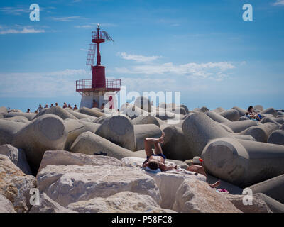 Chioggia, Italien - 23. Juni 2018: Rote Leuchtturm, der den Eingang des Hafens und der Menschen, die auf den Felsen tan zeigt. Stockfoto