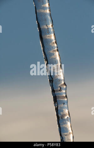 Vertikale Nahaufnahme des langen, schlanken Eiszapfen mit Hintergrund der blauen Himmel und Licht, hohe Wolke. In der Lage zu sehen, Bändern und Texturen in der eiszapfen. Stockfoto