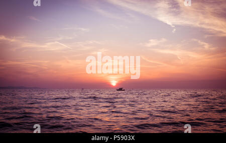 Sonnenuntergang am Meer vom Strand aus gesehen. Ein Boot auf dem Meer vor der Dämmerung Himmel wie die Sonne in Zadar, Kroatien. Ende Mai 2018 genommen. Stockfoto