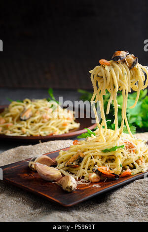 Italienische Pasta in einer cremigen Sauce mit Fisch, Garnelen und Muscheln auf eine Gabel auf einem dunklen Hintergrund Stockfoto