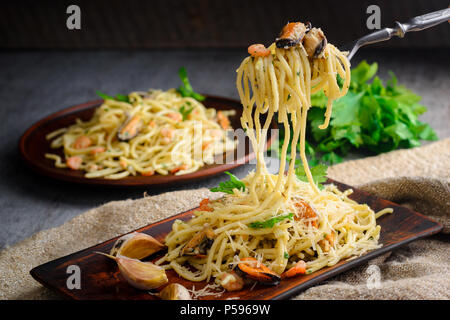 Italienische Pasta in einer cremigen Sauce mit Fisch, Garnelen und Muscheln auf einer Platte auf einem dunklen Hintergrund Stockfoto