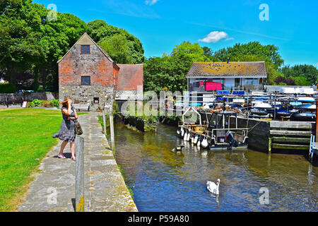 Eine Dame Spaziergänge entlang der Kante des Kai vor Ort Mühle Wassermühle, die sich dort befinden, wo die Flüsse Stour & Avon im Town Quay, Christchurch, Dorset treffen Stockfoto