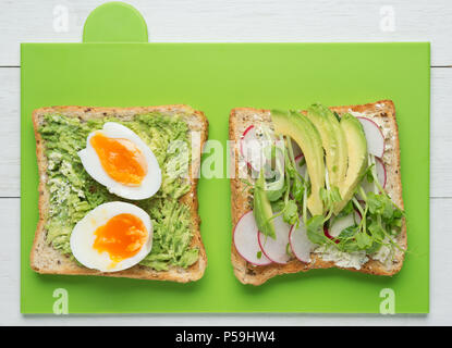 Zwei avocado Toasts mit weich gekochte Eier, Guacamole, geschnitten, Avocado, Rettich, Schnee Erbse Sprossen und Ziegenkäse Stockfoto