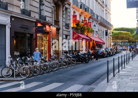 Paris, Frankreich, 9. August 2017. Schmale Französische Straße in Paris mit Restaurant, Boutique, geparkten Fahrräder und Motorroller in der Abenddämmerung. Rue Cambon, klassische seine Stockfoto