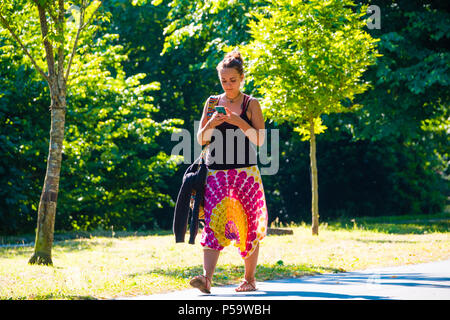 Aberystwyth, Großbritannien. 26 Juni, 2018. UK UK Wetter: Eine junge Frau sucht ihre Telefone beim Spaziergang im Park in Aberystwyth zu Beginn der dennoch einen anderen Tag der heißen Sonne ungebrochen. Das Vereinigte Königreich ist die Überschrift in eine mini Hitzewelle mit Temperaturen um 29° oder 30° Celsius bis Mitte der Woche Foto: Keith Morris/Alamy leben Nachrichten Stockfoto