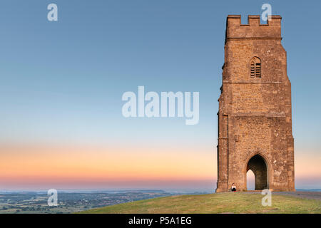 Glastonbury, Somerset, UK. 26 Juni, 2018. UK Wetter - saß oben auf der Glastonbury Tor, eine junge Dame Uhren einen wunderschönen Sonnenaufgang über der Somerset Levels, wie der Westen von England wird eingestellt, um zu sehen, Temperaturen wieder in der 20er Jahre steigen. Credit: Terry Mathews/Alamy leben Nachrichten Stockfoto