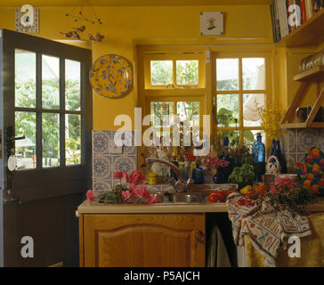 Sommer Blumen im Waschbecken unter Fenster in Yellow Cottage Küche mit Hälfte verglaste Tür Stockfoto