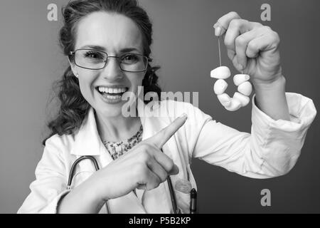 Lächelnd Kinderarzt Frau in Weißem medizinischen Gewand zeigen auf Knoblauch Perlen auf isolierte Stockfoto