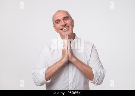 Closeup Portrait von verzweifelten reifer Mann im weißen Hemd mit gefalteten Händen, um Hilfe zu bitten oder zu entschuldigen. Stockfoto