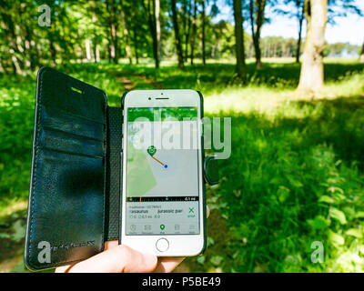 Nahaufnahme der Hand einer Frau, die ein Mobiltelefon mit einer Geocaching-App hält, die einen Cache in der Nähe mit verschwommenem Landweg zeigt, Schottland, Großbritannien Stockfoto