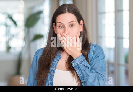 Junge schöne Frau zu Hause decken den Mund mit der Hand mit Schande für den Fehler, den Ausdruck von Angst erschüttert, die in der Stille Angst, geheime Konzept Stockfoto