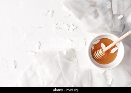 Flach von Honig in kleine keramische Schüssel, Holz- Honig Pendelarm, Seide und Blütenblätter auf einen weißen Hintergrund mit kopieren. Ansicht von oben. Stockfoto