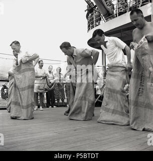 1950er Jahre, die Zeit zu verbringen, Spaß zu haben und aktiv bleiben, während Sie auf eine lange Reise, auf eine Union - Schloss Dampfer unterwegs zum Kap in Südafrika, erwachsenen männlichen Passagiere bereit, an einem Spiel teilzunehmen, die traditionellen Sackhüpfen, wo Kandidaten in Säcken oder Postsäcken hop von einem Ausgangspunkt zu einem Fertig stellen. Stockfoto