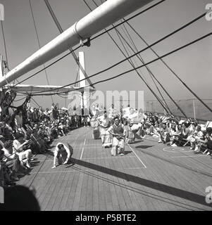 1950er Jahre, die Zeit zu verbringen, Spaß zu haben und aktiv bleiben, während Sie auf eine lange Reise, eine Union - Schloss Dampfer unterwegs zum Kap in Südafrika, erwachsenen männlichen Passagiere an einem Spiel nehmen, den traditionellen Sackhüpfen, wo Kandidaten in Säcken oder Postsäcken hop von einem Ausgangspunkt zu einem Fertig stellen. Andere Passagiere in Liegestühlen jubeln Ihnen zu sitzen. Stockfoto