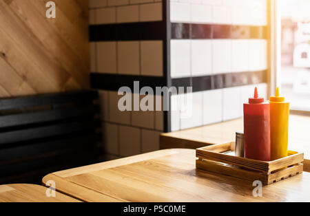 Ketchup und Senf Flaschen auf dem Tisch. Die Flaschen sind auf den Fokus, Sitzbank ist verschwommen. Stockfoto