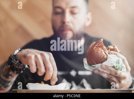 Junger bärtiger Mann essen Burger und Pommes frites. Stockfoto