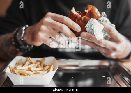 Junger bärtiger Mann essen Burger und Pommes frites. Stockfoto