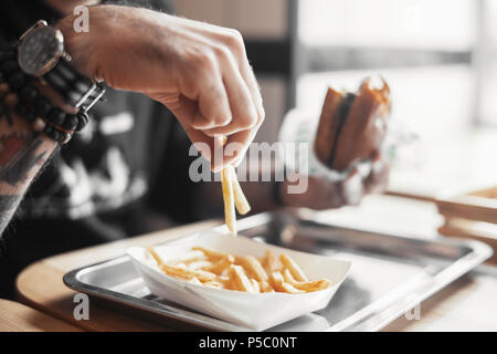 Junger bärtiger Mann essen Burger und Pommes frites. Stockfoto